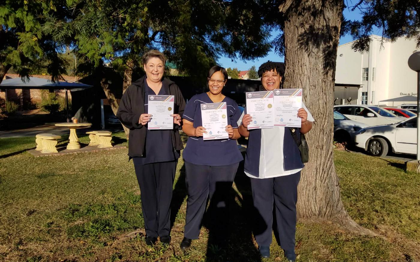 Three graduates holding certificates under a tree